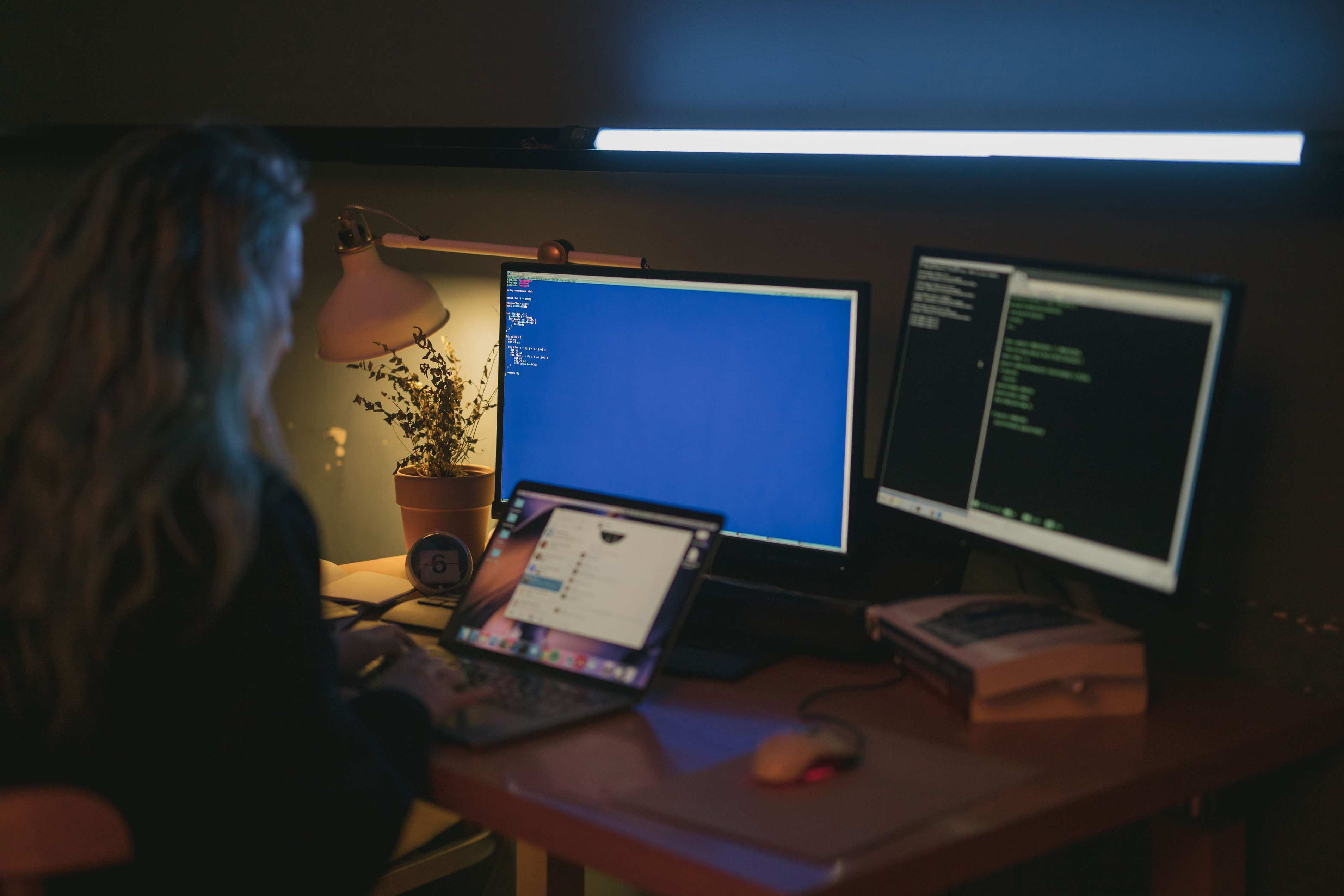 Abendlich beleuchteter Schreibtisch mit Laptop, Monitor und mehreren Bildschirmen in einem Homeoffice